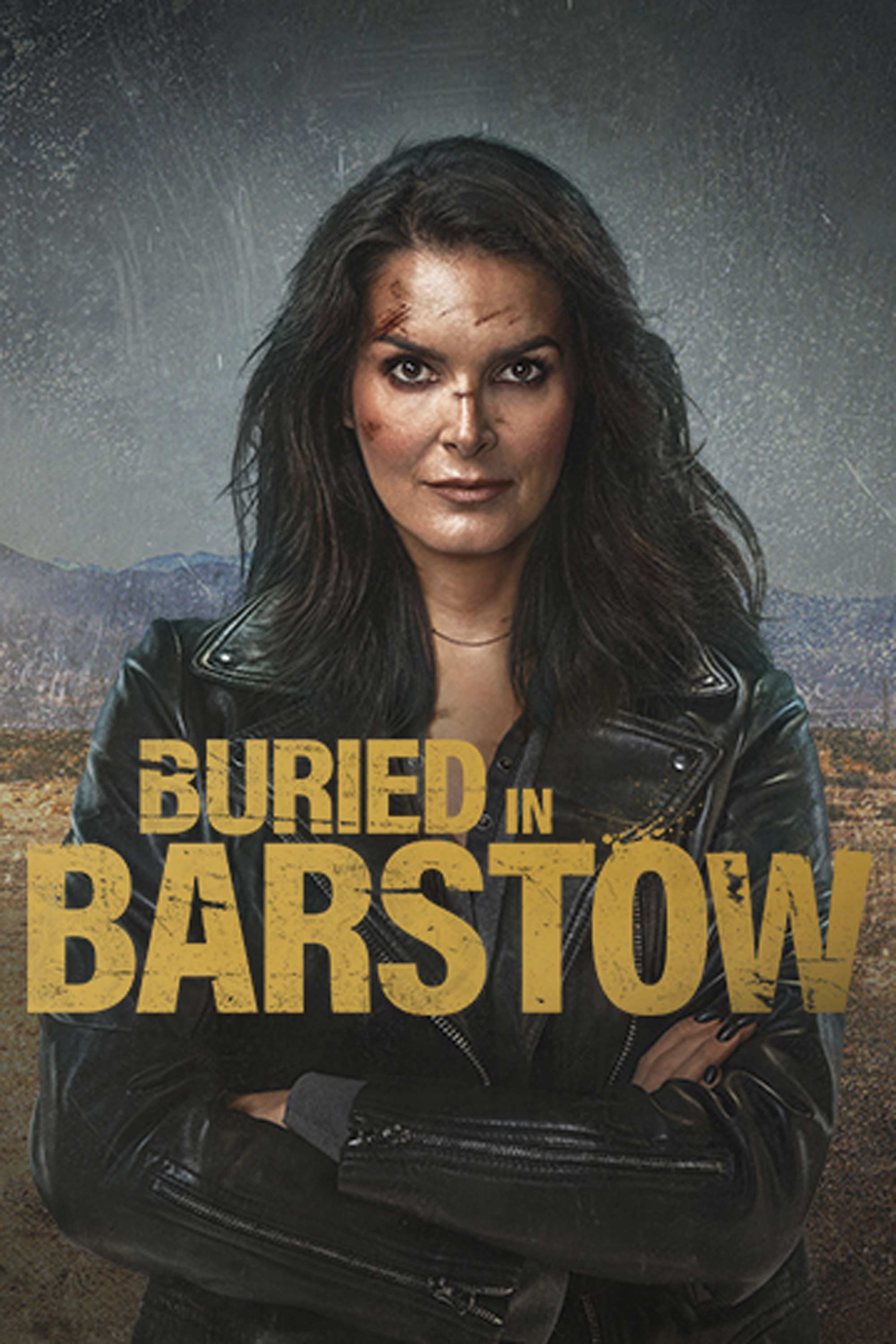 Angie Harmon with facial cuts and arms crossed in a black leather jacket for Buried in Barstow in a desert landscape.