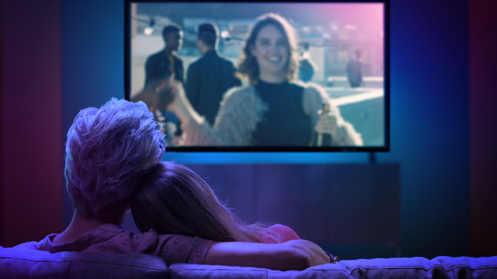 Two people sitting on a couch watching TV